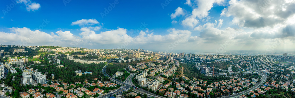Aerial panorama of Ramot Remez and Romema modern neighborhoods with major intersecting roads modern houses with white walls and red roofs, high rising new construction in Haifa Israel with blue sky