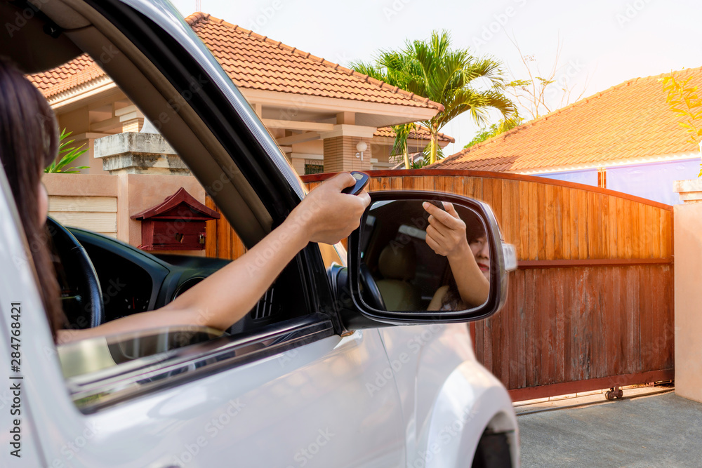 Ταπετσαρία Woman in car, hand using remote control to open auto wooden door with modern home blurred background