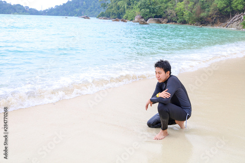 Happy man setting on a beach at Surin Islands, archipelago of five islands in the Andaman Sea. Attraction tourist in Thailand with blue sea.