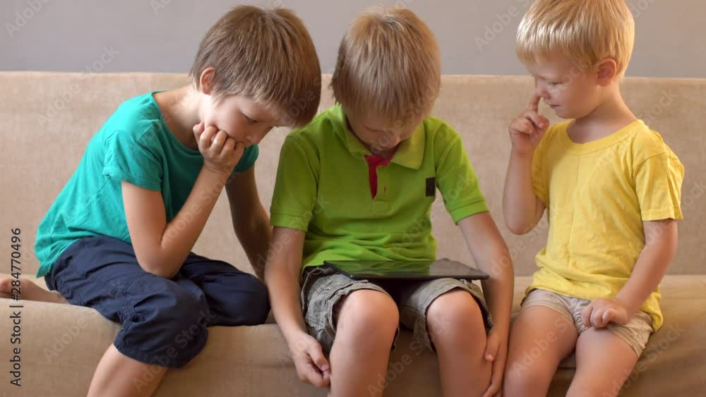 Happy calm children are playing with tablet. boys are happy together on vacation at their parents' house. Friendly joint preparation for school. Happy calm children are playing with tablet. boys are happy together on vacation at their parents' house. Friendly joint preparation for school.