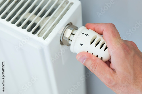 Hand adjusting thermostat valve of heating radiator in a room.