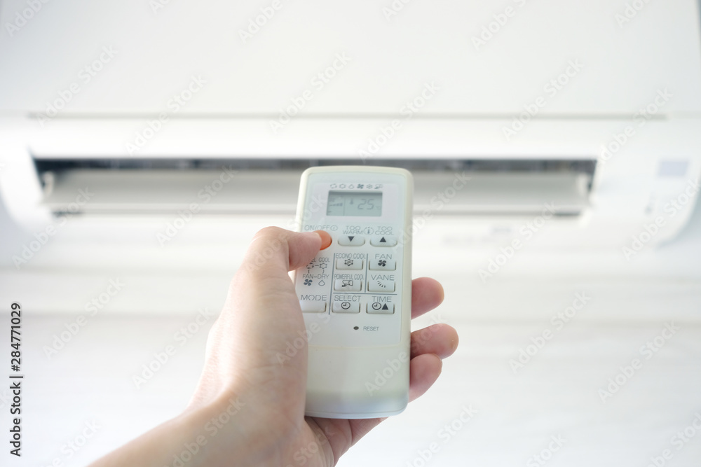 Man's hand using remote control open The air conditioner is cooled to 25 degrees Celsius in his bedroom. Health concepts and energy savings Man's hand using remote control open The air conditioner is cooled to 25 degrees Celsius in his bedroom. Health concepts and energy savings