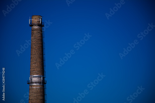 Old brick factory pipe with smoke-free antennas GSM on blue sky background. Concept pollution of environment, emissions into water resources, oncological diseases, cancer.
