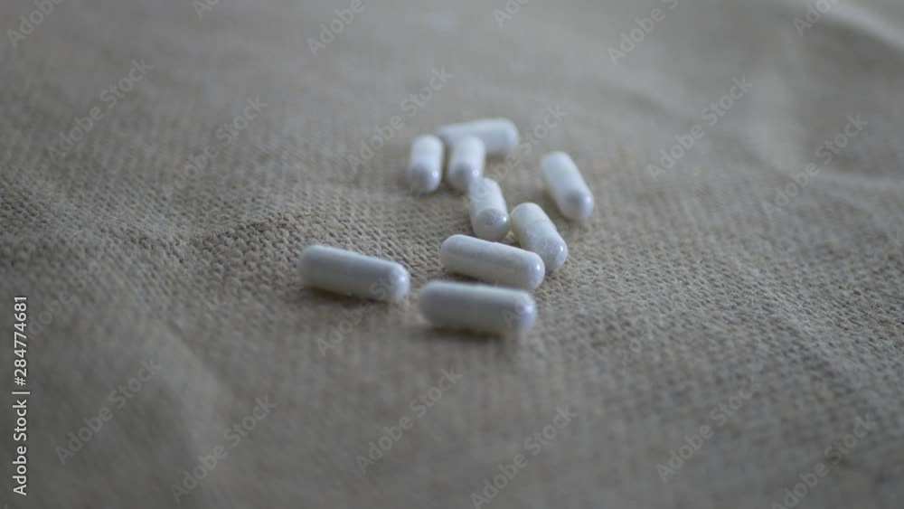 White medicinal pills falling on sackcloth material close up footage. White medicinal pills falling on sackcloth material close up footage.
