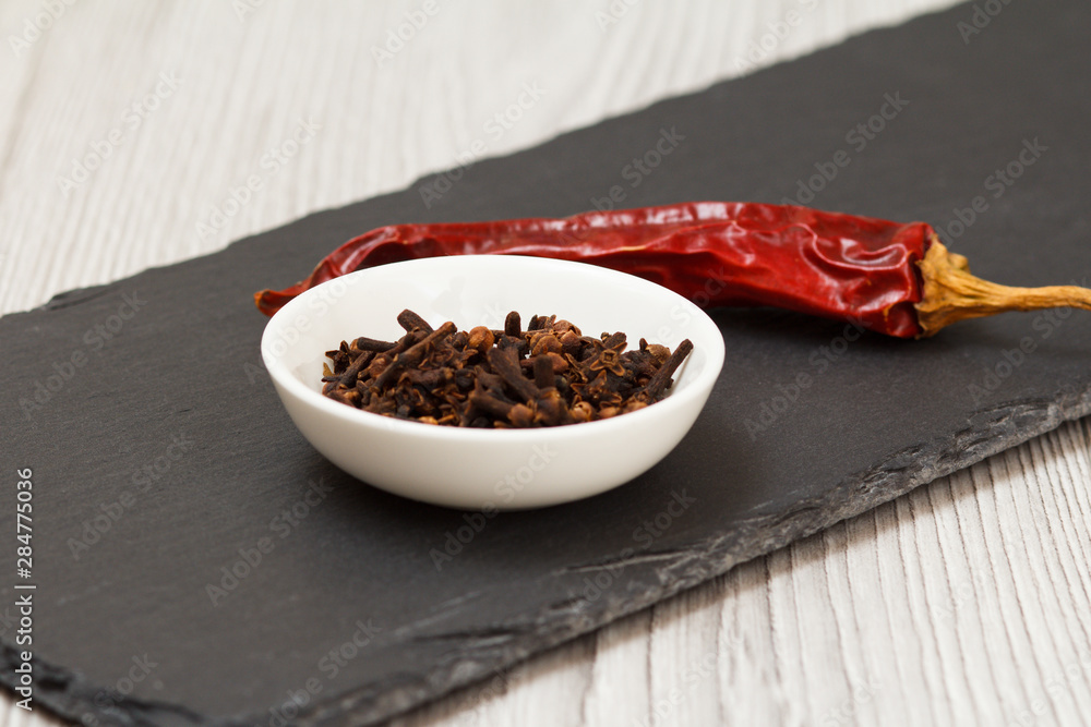 Cloves in a bowl and dry red pepper on stone cutting board Cloves in a bowl and dry red pepper on stone cutting board