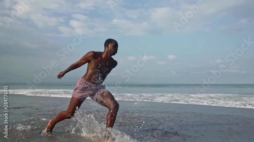 Contemporary ballet dancer performing at the beach. Real time and slow motion combined gimbal shot on young attractive and athletic black African American man dancing by the sea