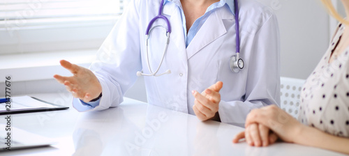 Doctor and patient discussing something while sitting at the desk at hospital, close-up. Medicine and health care