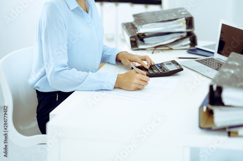 Unknown female bookkeeper or financial inspector calculating or checking balance, making report, close-up. Internal Revenue Service at work with financial document. Tax and audit concept