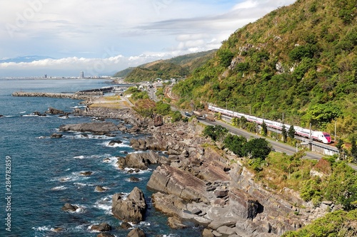 Scenery of a beautiful beach in Beiguan Tidal Park in Toucheng, Yilan, Taiwan, with an express train traveling on the railway by the green mountainside and a coast highway along the rocky coastline photo