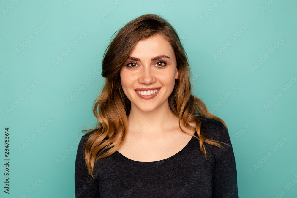 Portrait of smiling young lady with white teeth standing in a studio isolated over the blue background. Portrait of smiling young lady with white teeth standing in a studio isolated over the blue background.