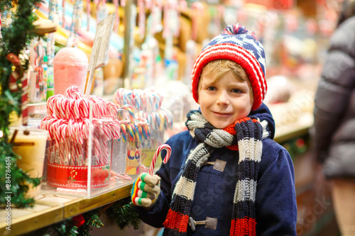 Little cute kid boy buying sweets from a cancy stand on Christmas market. Happy child on traditional family market in Germany. Preschooler in colorful winter clothes photo