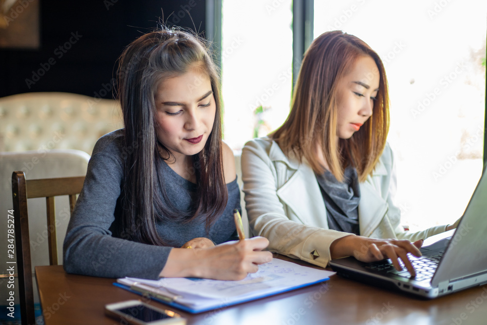 Two Asian business women using notebook working and Discussion of the important contract at office Two Asian business women using notebook working and Discussion of the important contract at office