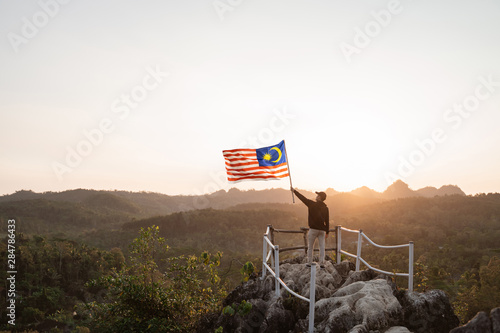 asian man with malaysian flag of malaysia on top of the mountain photo