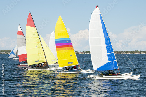Children close sailing, racing catamarans with brightly coloured sails.