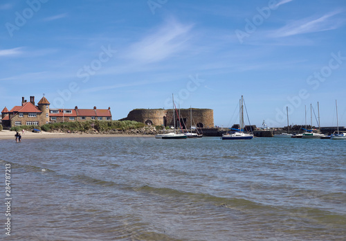 Looking North towards the Harbour at Beadnell Bay, with people Paddling in the Sea, and Yachts anchored next to the Breakwater, Northumberland, England.
