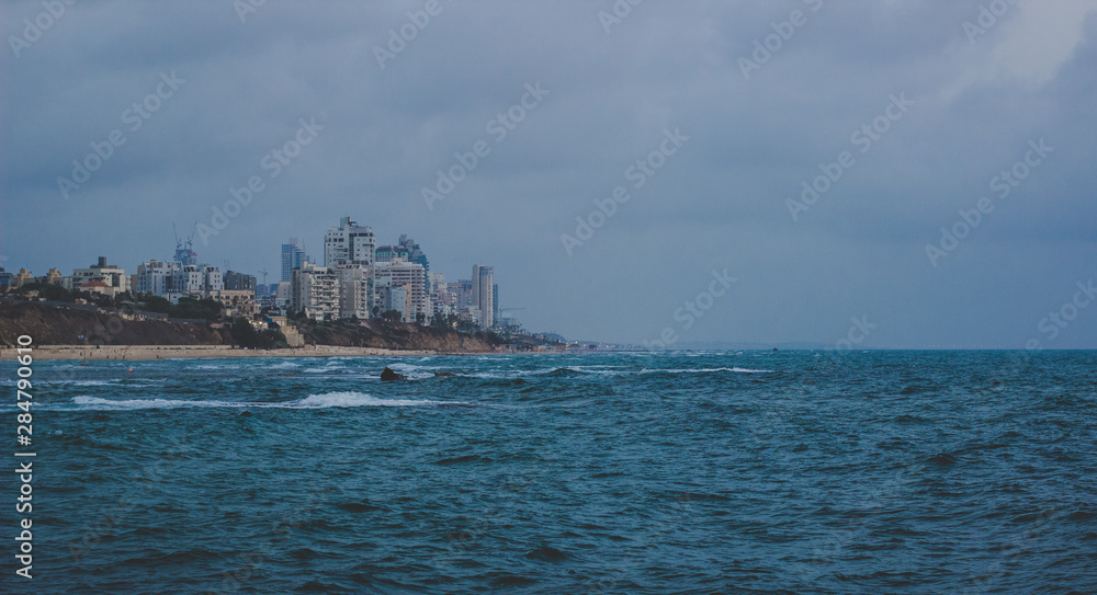 Mediterranean seafront port modern city landmark view with skyscrapers photography with stormy and wavy water surface foreground in cloudy and rainy weather time 