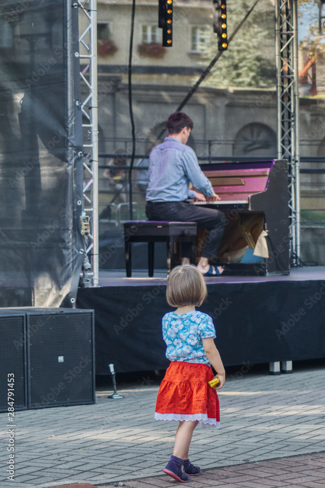 dziewczynka zasłuchana w muzyce spogląda na pianistę na plenerowym koncercie