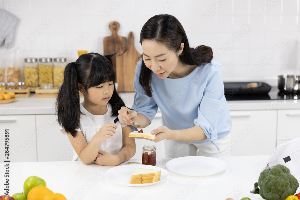 Happy Asian family Mother and daughter helped to make breakfast in the kitchen at home. Bread with jam. Family Cooking concept Happy Asian family Mother and daughter helped to make breakfast in the kitchen at home. Bread with jam. Family Cooking concept