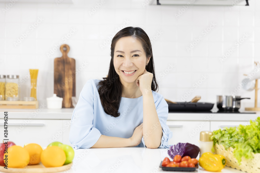 Portrait of Asian woman Smiling at you in the kitchen and salad ingredients on table at home. Healthy women and Healthy food concept