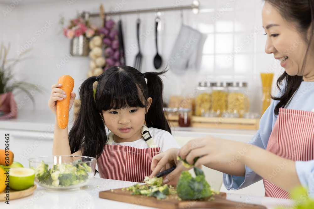 Happy Asian family Mother and child daughter are preparing the salad and cutting vegetables. cooking food in kitchen at home. Healthy food concept