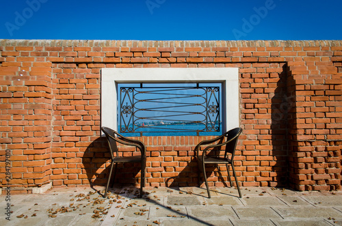 Due sedie uguali davanti a un muro di mattoni con una finestra che si affaccia sulla laguna di Venezia