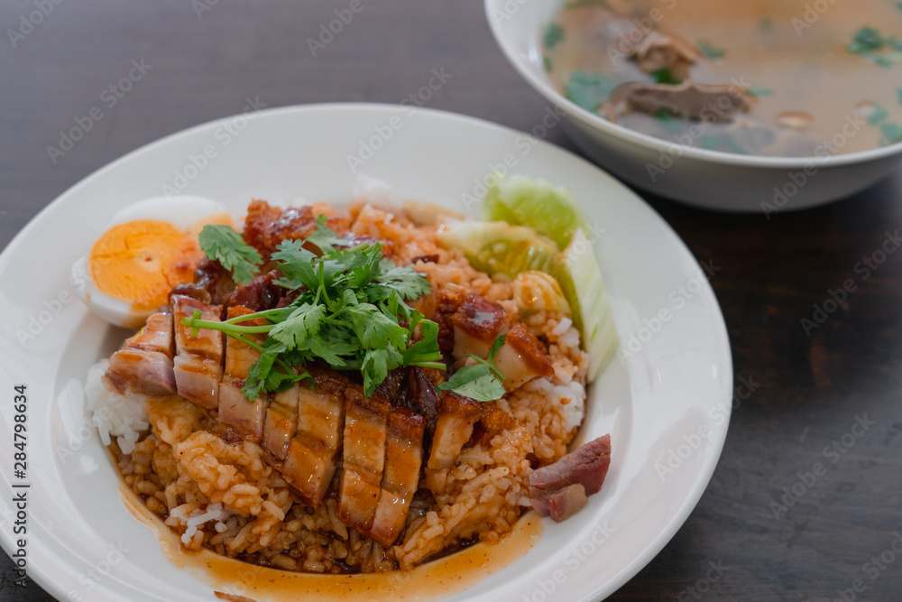 Close up rice crispy pork, roasted red pork, Scallion and boiled egg with sauce in white plate on wooden table background. Close up rice crispy pork, roasted red pork, Scallion and boiled egg with sauce in white plate on wooden table background.