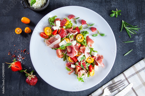 Close up view on fresh, summer salad with cherry tomato, strawberry, jamon and microgreen. Tasty food flat lay. Food for healthy and delicious lunch. Copy space. Top view