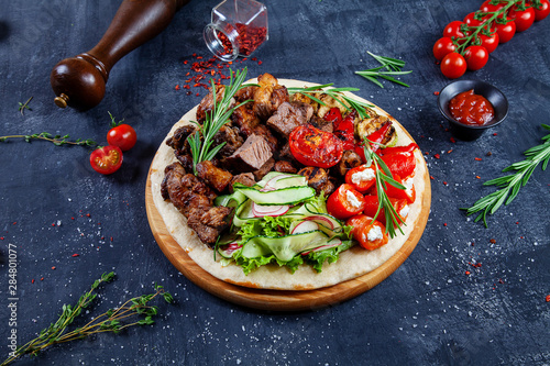 Close up view on tasty grilled meat with vegetables on georgian pita. shashlik or barbecue meat on pita. Shish kebab, traditional georgian cuisine food. Copy space for design. Dark background