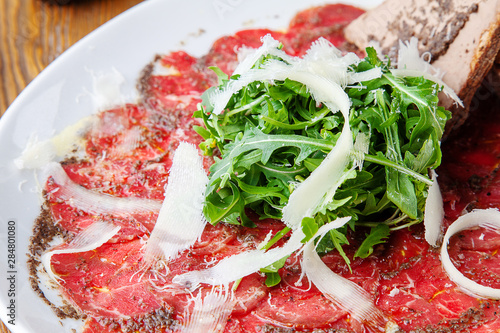 Delicious selective focus on veal (beef, meat) carpaccio with arugula and parmesan in white plate. Close up. Tasty dish of italian cuisine. Food photo for menu or banner