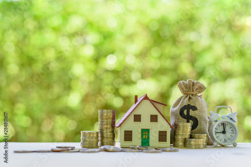 Residential real estate loan, financial concept : House model, coins, US dollar bag, white clock on a table, depicts home loan or borrowing money to buy / purchase a new home for first time homebuyer photo