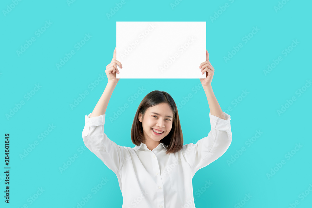 Young Asian woman holding blank paper with smiling face and looking on the blue background. for advertising signs. Young Asian woman holding blank paper with smiling face and looking on the blue background. for advertising signs.