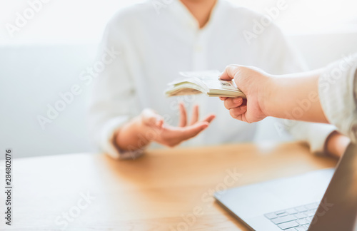 Close-up of hands giving dollar pay compensation from work. Give rewards as incentives for work, on office desk background. photo