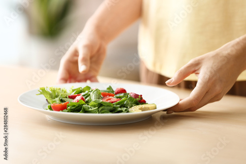 Fototapeta Naklejka Na Ścianę i Meble -  Woman with fresh salad on plate at table, closeup