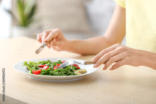Woman eating fresh salad with strawberry and spinach at table