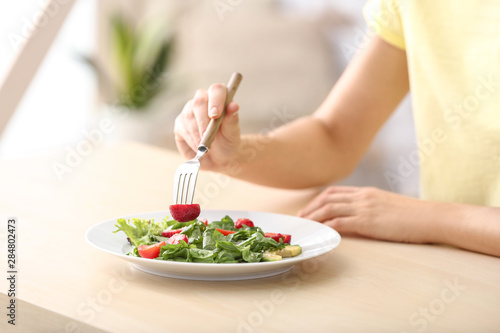 Woman eating fresh salad with strawberry and spinach at table