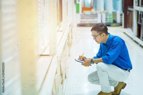 Asian manager man doing stocktaking of products in cardboard box on shelves in warehouse using digital tablet and pen.  photo