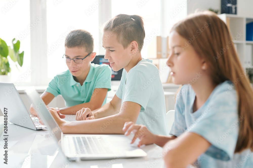 Three young schoolkids in casualwear sitting in computer classroom Three young schoolkids in casualwear sitting in computer classroom