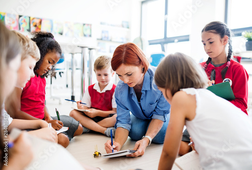 Tableau sur toile A group of small school kids with teacher sitting on the floor in class, learning