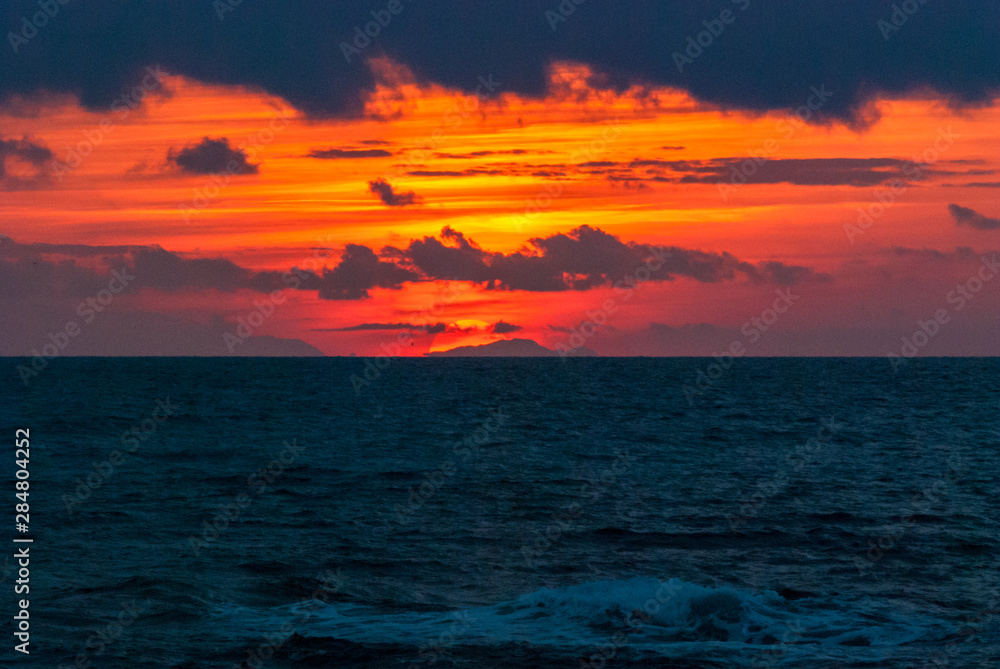 Gli ultimi raggi del sole che tramonta dietro un cielo pieno di nuvole rosse visti da Livorno