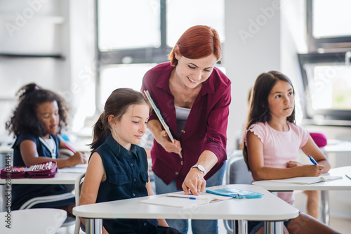 A teacher walking among small school children on the lesson, explaining.