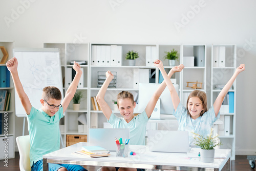 Three successful schoolmates keeping their hands raised while expressing joy