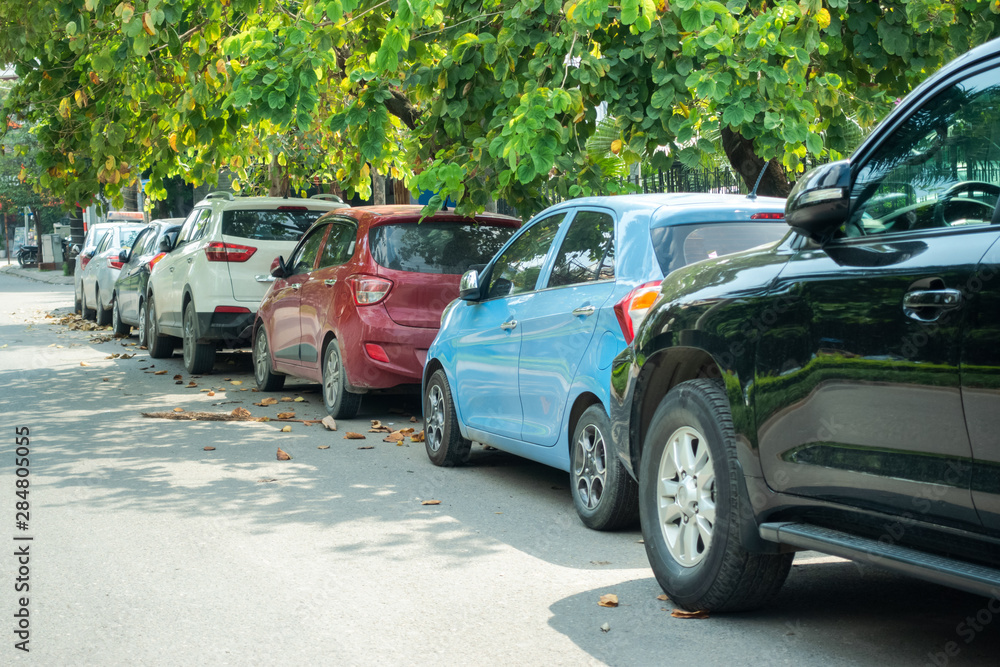 Fototapeta premium Parallel cars parking on street with green trees