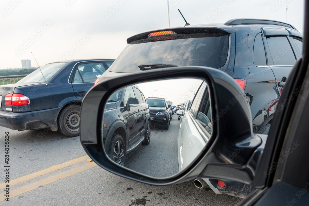 Reflection of traffic flow in left side rear view mirror at rush hour