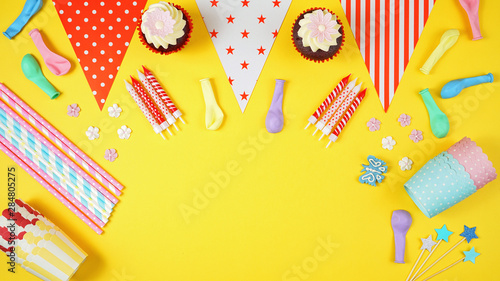 Colorful birthday party flat lay with party food, balloons, decorations and gifts on yellow background, with copy space.