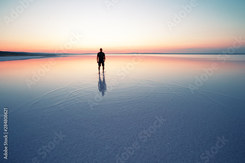 Silhouette of man departing into sunset on smooth water of lake