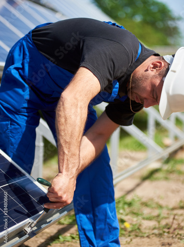 Technician working on exterior voltaic stand-alone solar panel system installation on bright sunny summer day. Renewable ecological cheap green energy production concept. photo