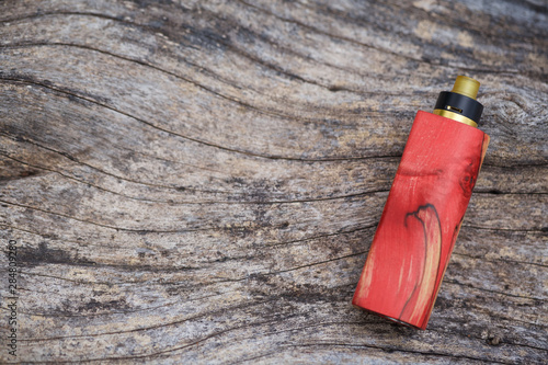 high end red natural stabilized wood regulated box mods with rebuildable dripping atomizer on natural timber wood texture background, vaporizer equipment, selective focus photo