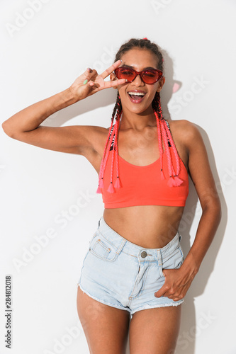 Positive cheerful young african woman posing isolated over white wall background wearing sunglasses showing peace gesture.