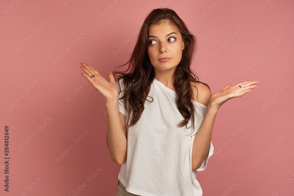 A girl in a white top is standing on a pink background, looking to the side with her arms outstretched. A girl in a white top is standing on a pink background, looking to the side with her arms outstretched.