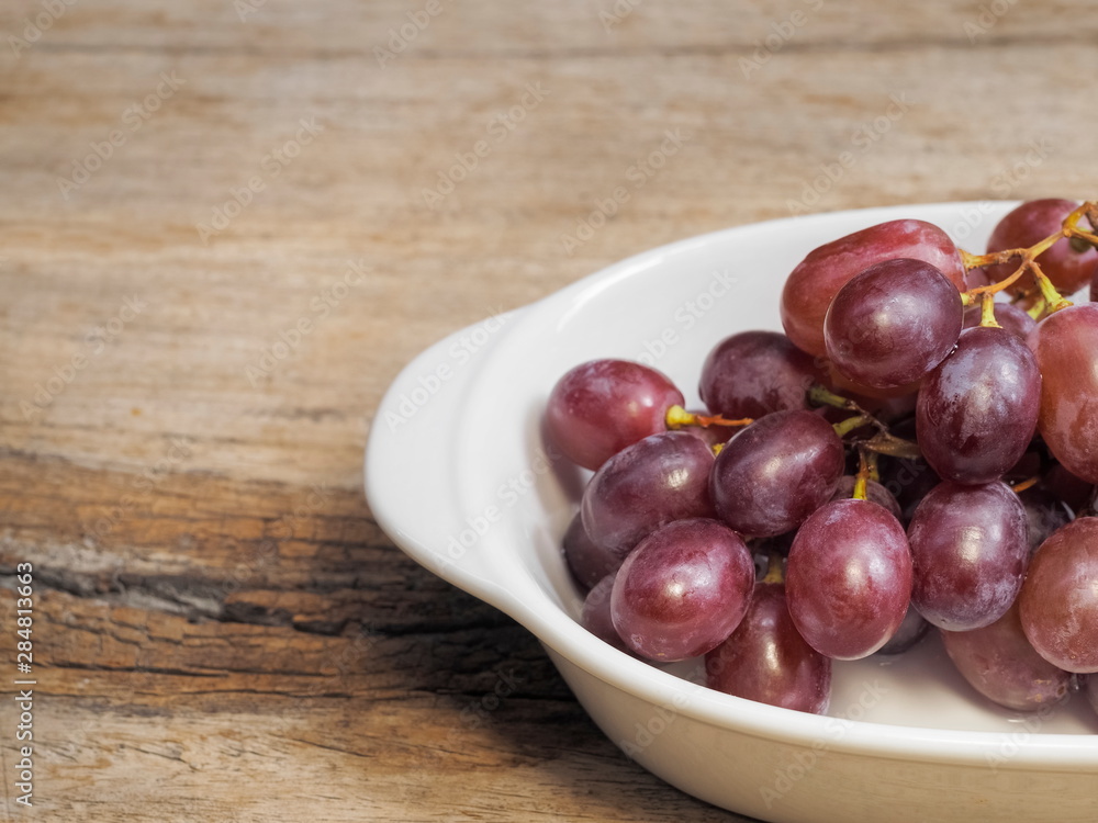 Close-up fresh red ripe grapes in white dish on wood texture background. Close-up fresh red ripe grapes in white dish on wood texture background.